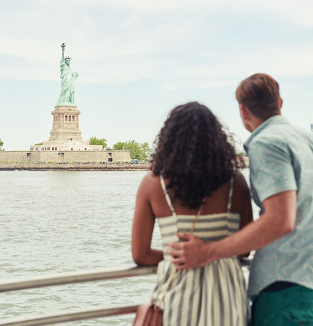 man and woman look at statue of liberty
